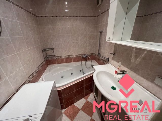 A bathroom with a corner bathtub and a sink in a 3-room apartment, tiles with a pattern.