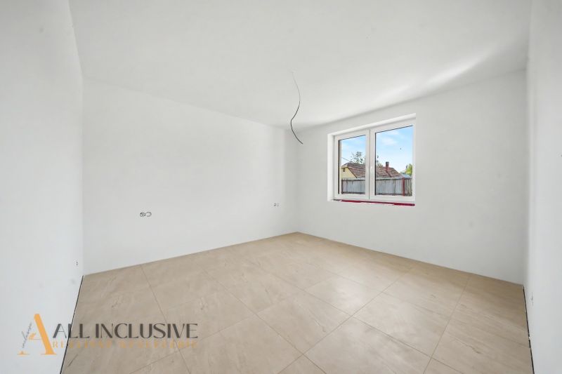 An empty room in a family house with a large window and a wooden-patterned floor.
