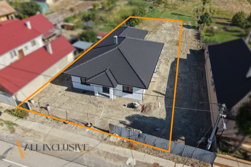 A family house in Tomášikovo with a dark roof and a fenced plot of land with planting.