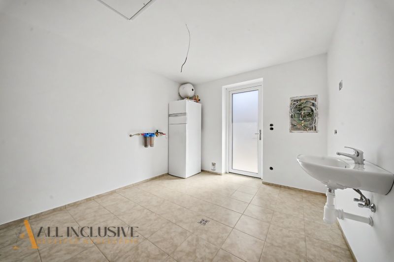 A view of the utility room in a family house with tiles and a sink.