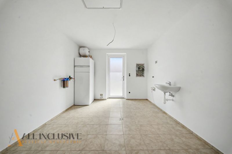 A white room in a family house with a sink and a boiler on the wall.