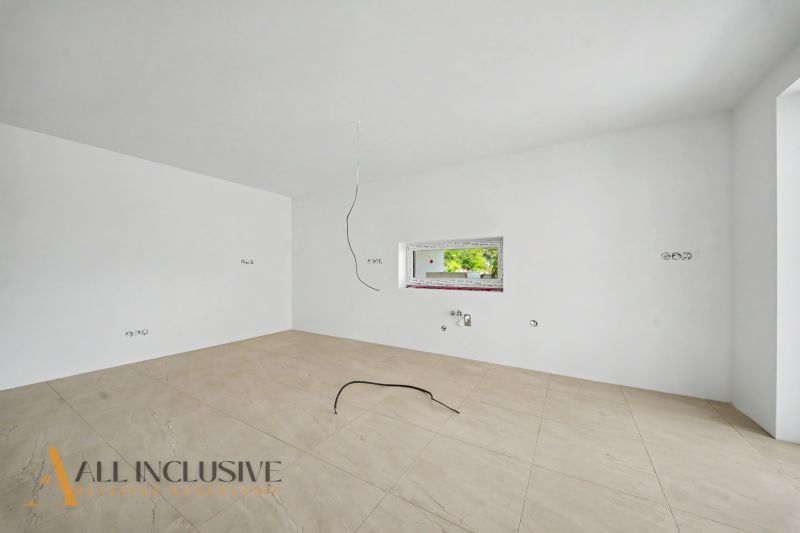 Empty room with white walls, a window, and a wooden-patterned floor in a family house.