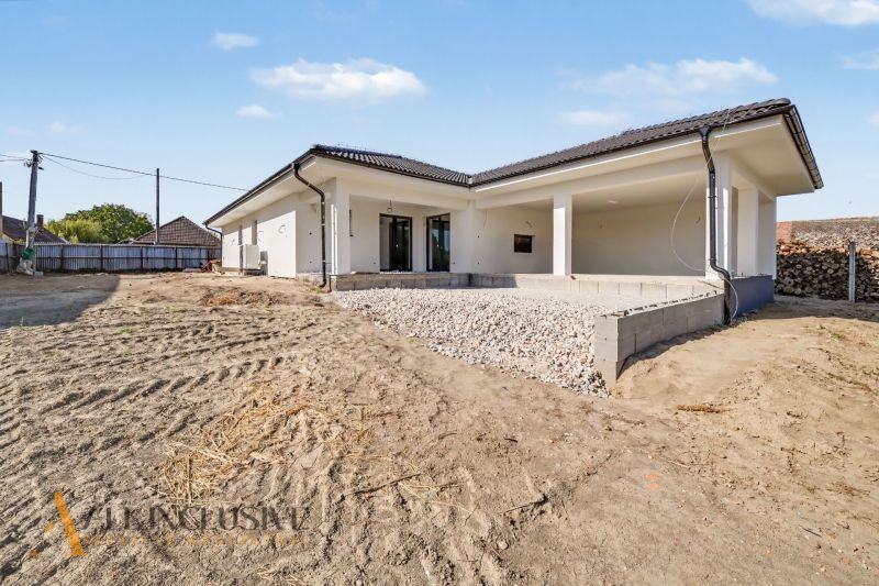 A family house in Tomášikovo with a terrace and an uneven plot under the blue sky.