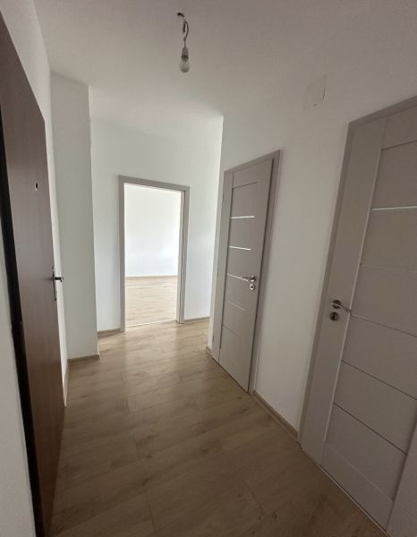 A hallway in a two-room apartment with a wooden decor floor and white walls.