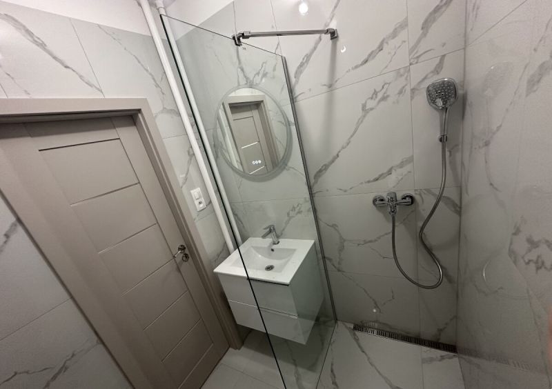 A bathroom with a shower and a sink in a 2-room apartment with a marble effect.