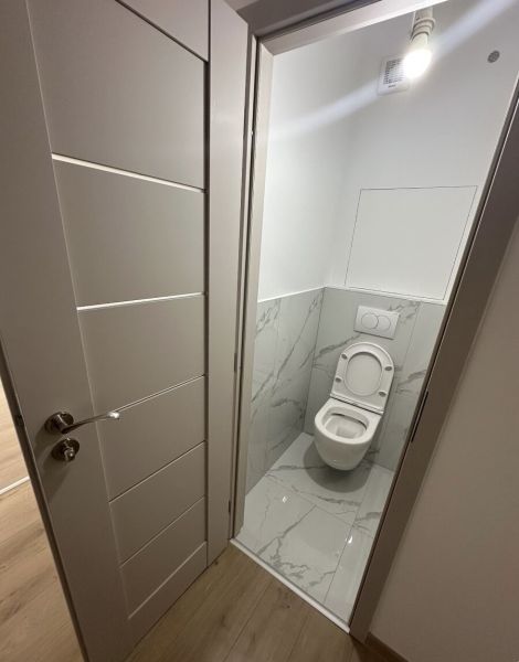 A toilet with white tiles and doors, and a floor with a wooden design.