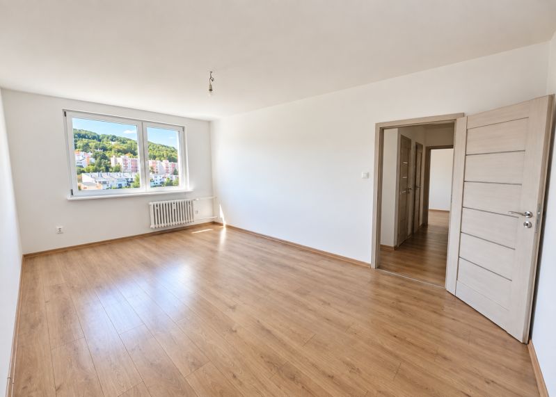 An empty room with a wooden floor, large windows, and white walls.