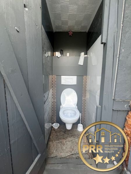 A toilet in a cabin, gray walls, decorative cladding, floor with wooden decor.