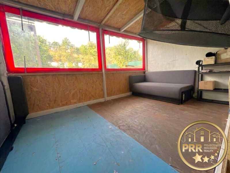 The attic of the cottage with windows and a wooden decor floor, a sofa, and shelves.