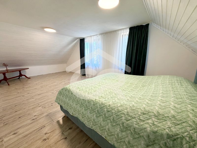 A bedroom in a family house with a wooden decor floor, a skylight, and a green blanket.