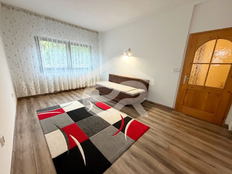 A room in a family house with a wooden decor floor, a carpet, a sofa bed, and curtains.
