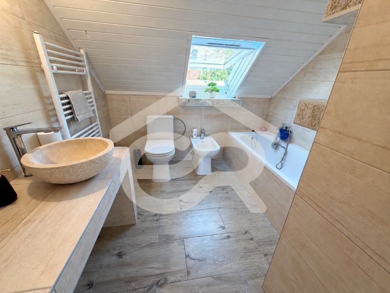 A bathroom in a family house with a bathtub, a sink, and a floor with a wooden decor.