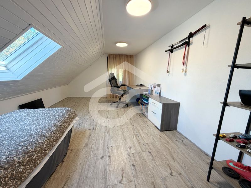 Attic room with wood-patterned flooring, a bed, and a desk in a family house.