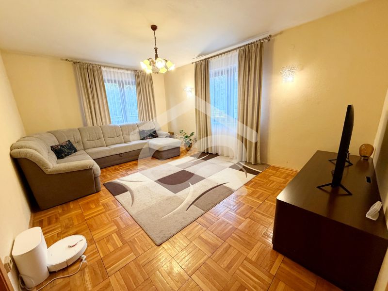 Living room with a corner sofa, carpet, and wooden decor flooring in a family house.