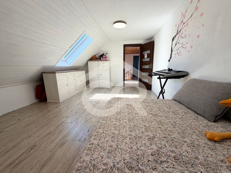The attic of a family house with a bed, dressers, and a skylight window, flooring with a wooden decor.