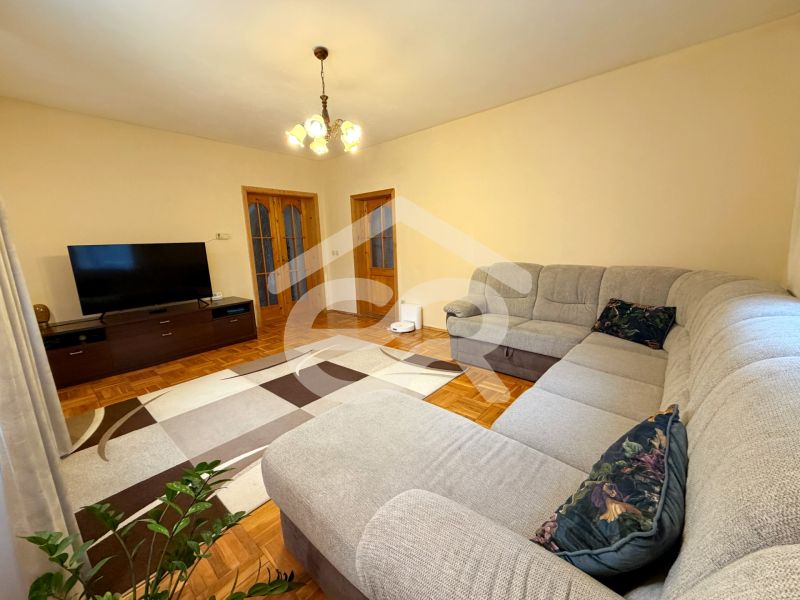 Living room with wood-patterned flooring, a large sofa, and a television in a family house.