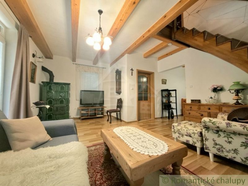 Living room in a cottage with wooden beams, wood-patterned flooring, and a stove.