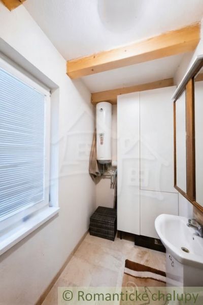 A bathroom in a cabin with a sink and a boiler, light walls and wooden beams.