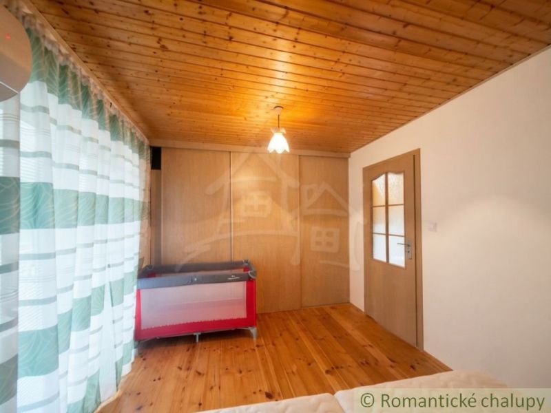 A room in a cabin with a wooden decor floor, a crib, and curtains.