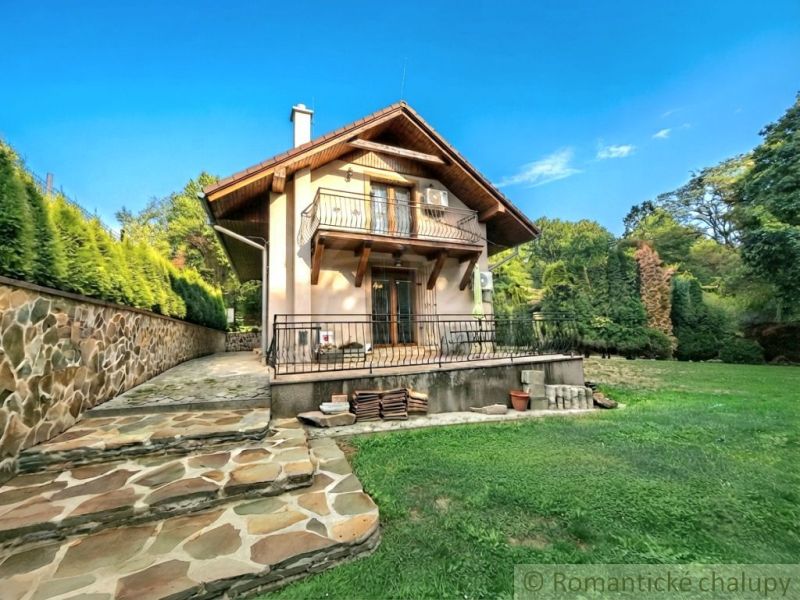 A cottage in Ružiná with a stone staircase and a lawn surrounded by greenery and a blue sky.
