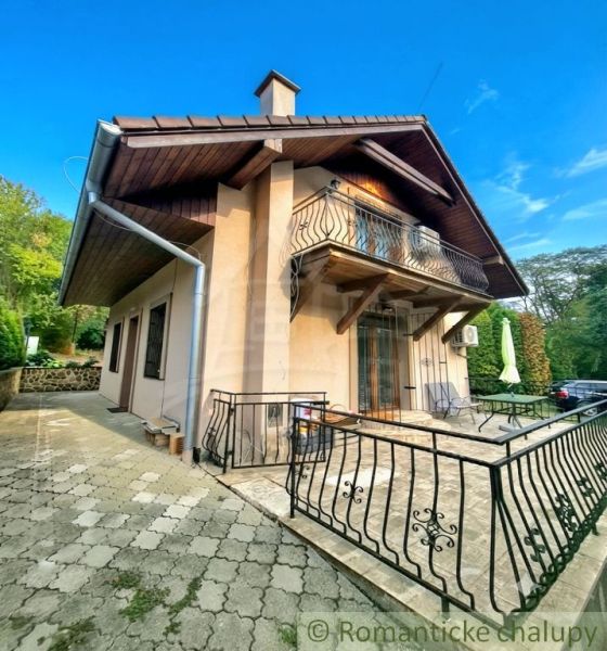 A cottage in Ružiná with a terrace and a balcony, surrounded by greenery and a blue sky.