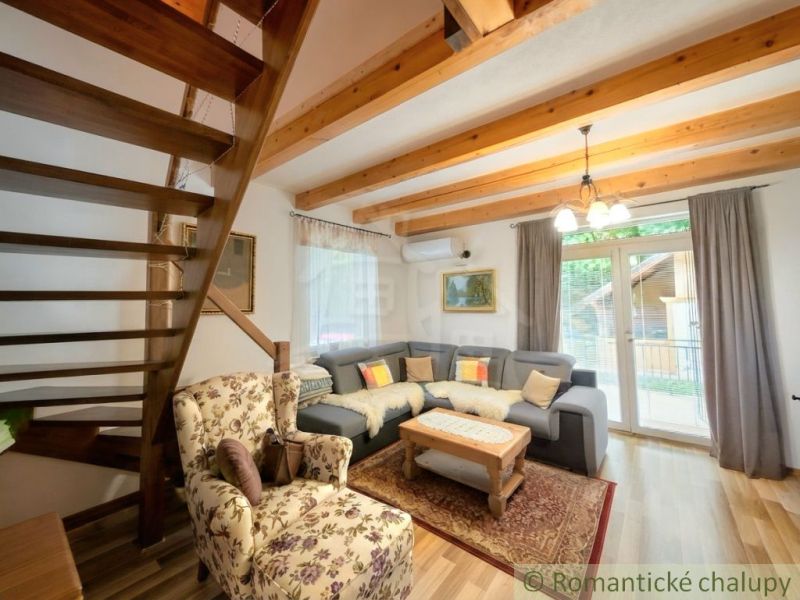 Living room in a cottage with wooden beams, a corner sofa, and a floral armchair.