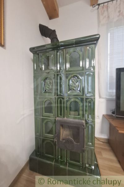 Traditional green ceramic stove in the interior of a cottage with a wood-patterned floor.