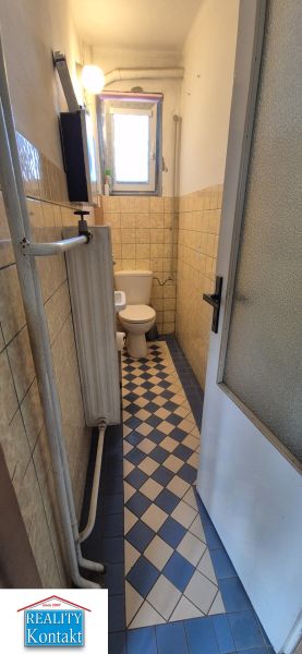 A narrow toilet in a family house with a radiator and patterned floor.