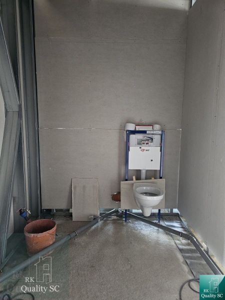 An unfinished bathroom in a family house with a mounted wall-hung toilet and preparation for tiling.