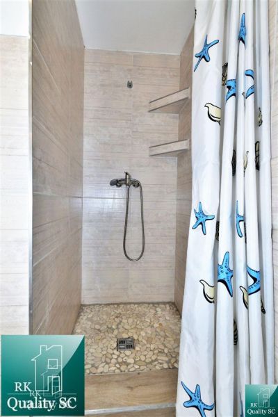 A shower corner with light tiles and a curtain with a sea motif in a cottage.