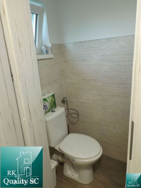 Bathroom in a cottage with a toilet, rectangular window, and wooden decor tiles.