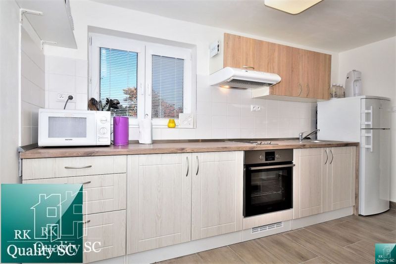 A kitchen in a cottage with white cabinets and appliances, flooring with a wood design.