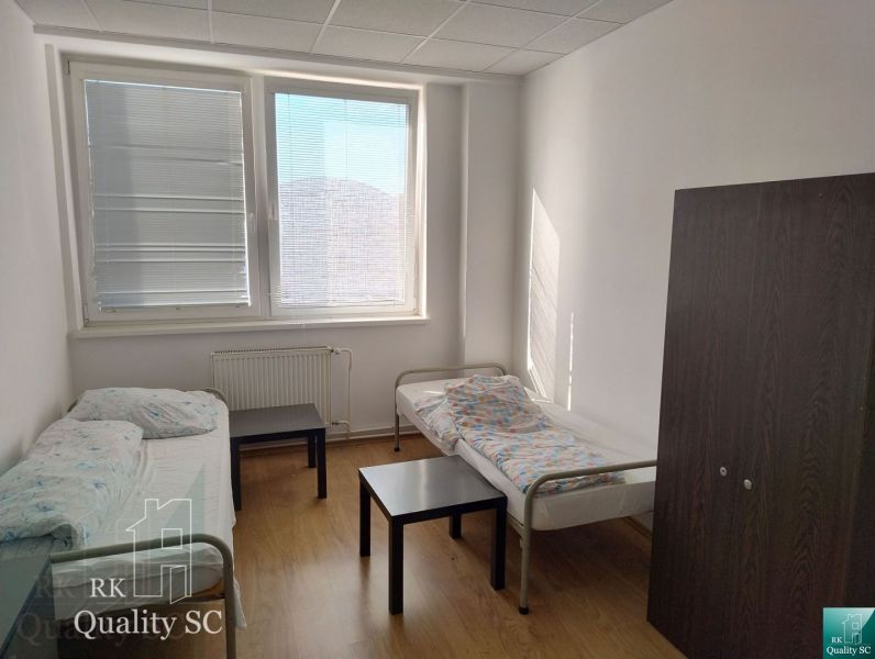 A room with two beds, a cabinet, a table, and a floor with a wooden decor.