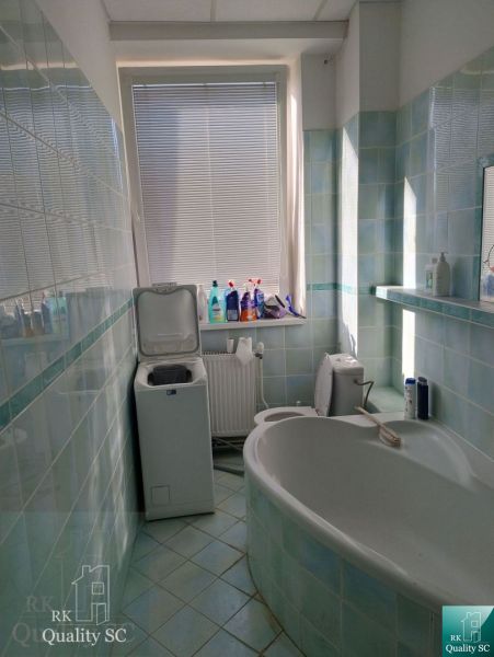A bathroom with a bathtub and a washing machine, tiled with light blue tiles.