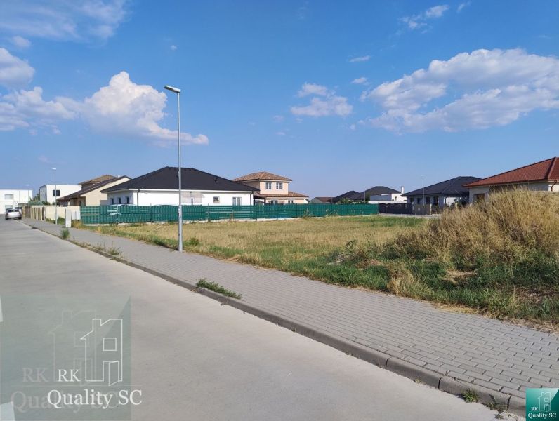 Residential plots in Senec surrounded by houses and greenery under a blue sky.