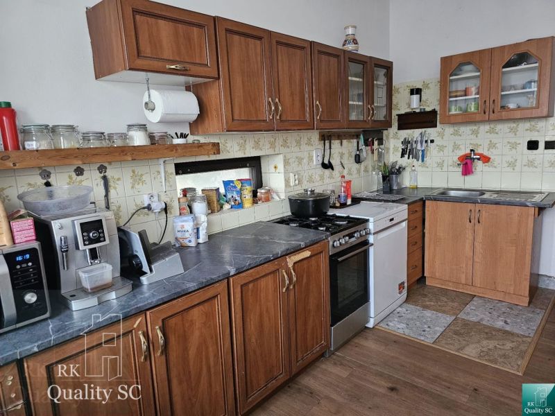 A kitchen in a family house with appliances, rustic cabinets, and a wood-patterned floor.
