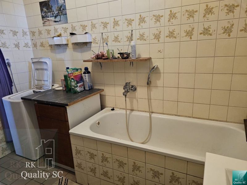 A bathroom in a family house with a bathtub, a washing machine, and tiles with a floral pattern.