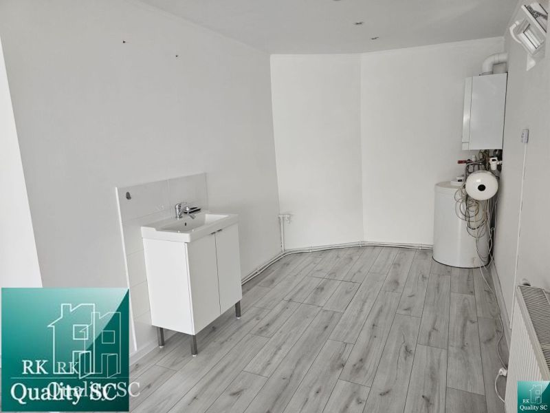 A white room with a sink, boiler, and wood-patterned flooring in commercial premises.