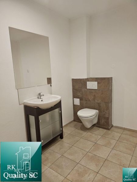 Bathroom commercial spaces with a sink and wall-hung toilet, light walls, tiles.