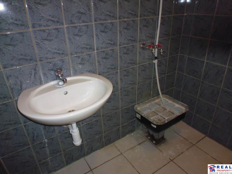 Bathroom in commercial premises with a ceramic sink and dark tiles on the walls.