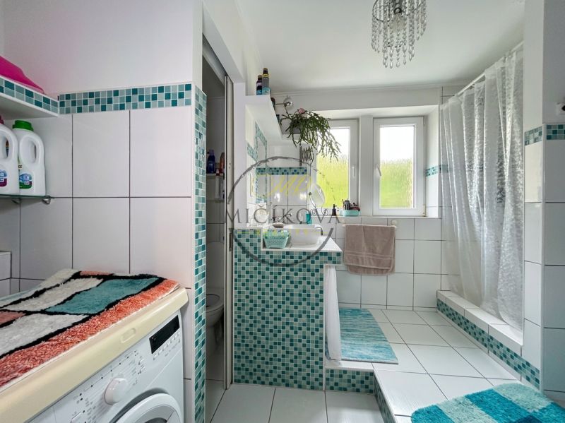A bathroom in a 2-room apartment with a shower, a washing machine, and blue tiles.