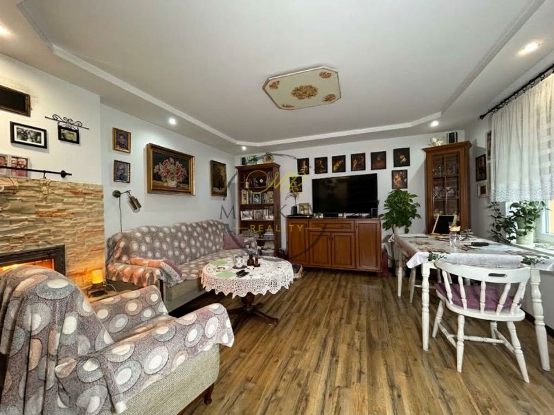 Living room with wood-patterned flooring in a two-room apartment, decorated with paintings and a fireplace.