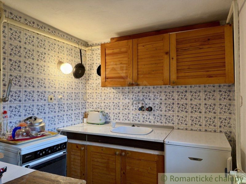 A kitchen in a cottage with wooden cabinets and tiles with a blue pattern.