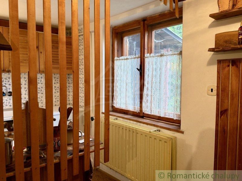 Interior of a cabin with wooden elements, a kitchen, and a window with curtains.