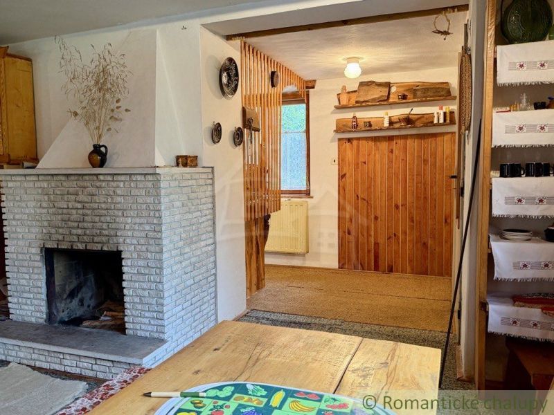 The interior of a cottage with a fireplace, wooden decorations, and shelves for plates and mugs.