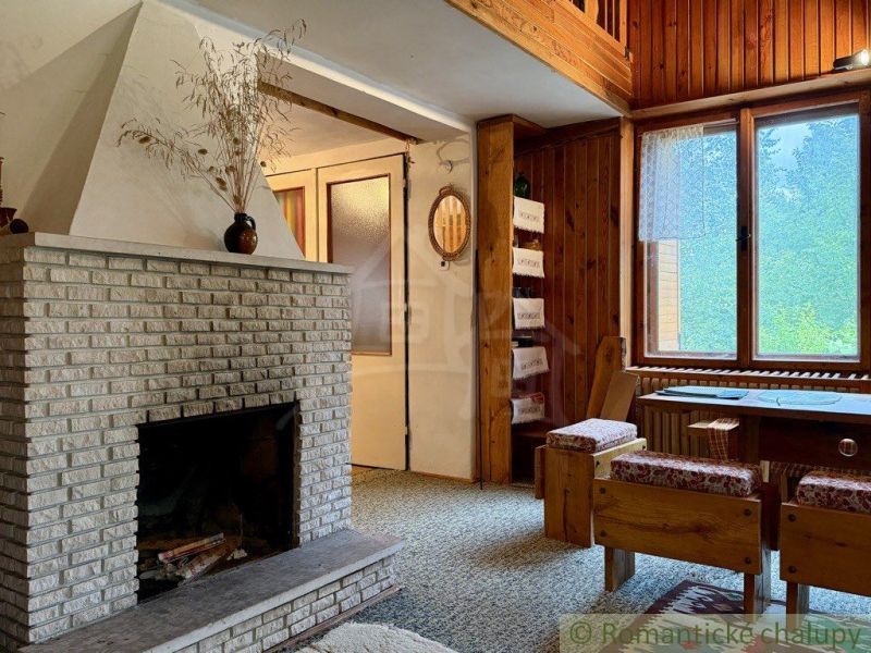 A cabin with a fireplace, wooden walls, and a large window, floor with a wooden decor.