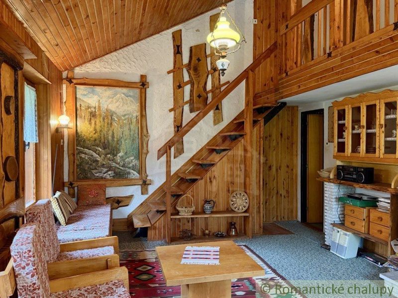 A cottage with wooden decor, armchairs, a painting on the wall, and a staircase leading to the upper floor.