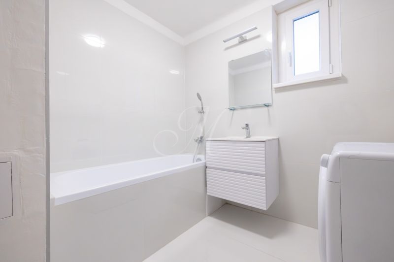 A bathroom in a 2-room apartment with a bathtub, a white sink, and a washing machine.