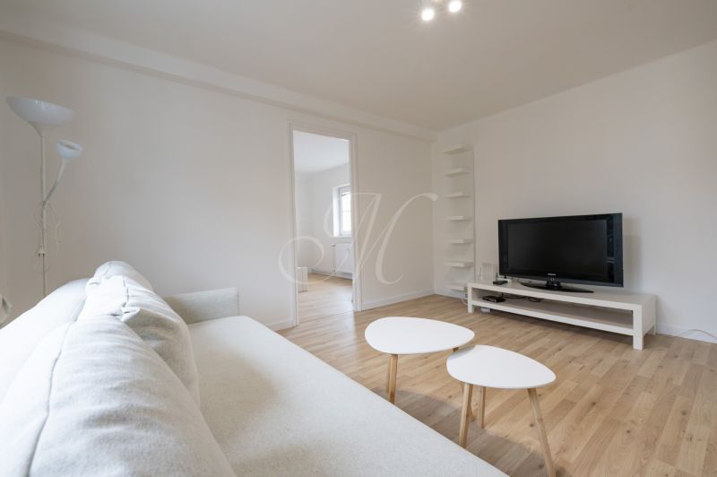 Living room in a two-room apartment with a wooden decor floor and white furniture.