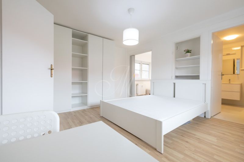 A bright bedroom with white furniture and a floor with a wood decor, in a two-room apartment.